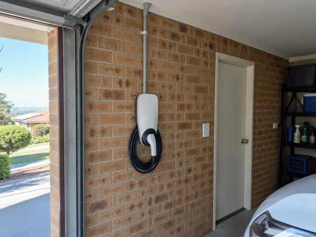 Wall-mounted EV charger on a brick garage wall beside a door and parked car in Bateau Bay