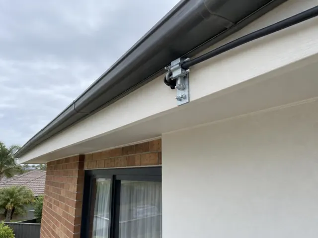 Overhead service cable and bracket mounted under a house eave on a brick exterior in Long Jetty